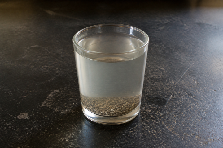 Black pepper powder sprinkled onto a glass of water, wetted and settled into an even dark layer on the bottom with the surface completely clear, the FSSAI at-home test for sawdust or bran filler in ground spices