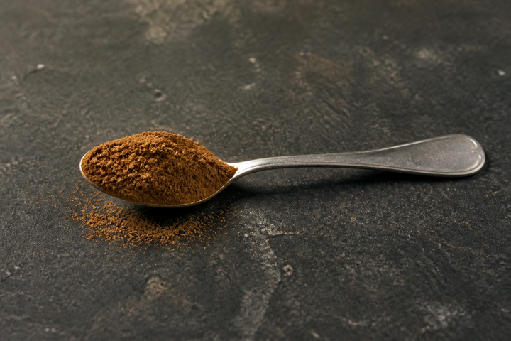 A steel spoon heaped with GetPured cinnamon powder on a dark stone counter, a warm reddish brown and fine in texture, ready for the at-home taste test that tells true cinnamon from cassia