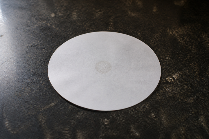A sheet of white filter paper where an oil spot has evaporated, leaving only a faint ring