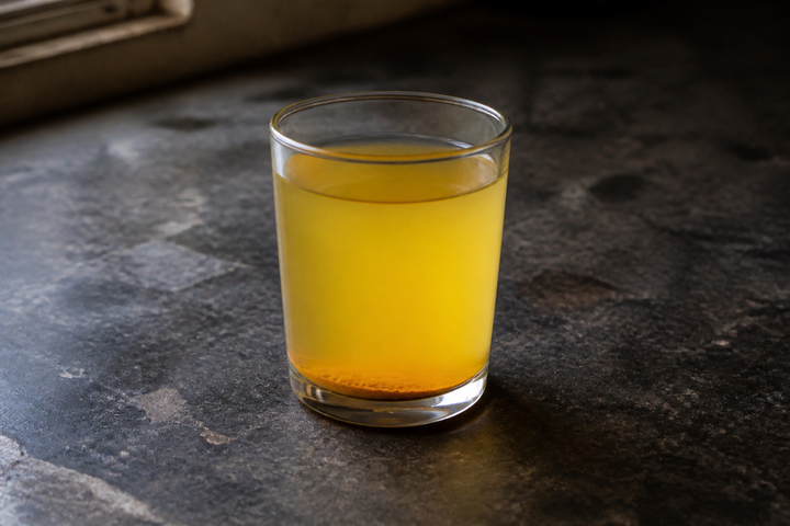 A glass of water with turmeric stirred in: the water a soft muted yellow, sediment settled on the bottom