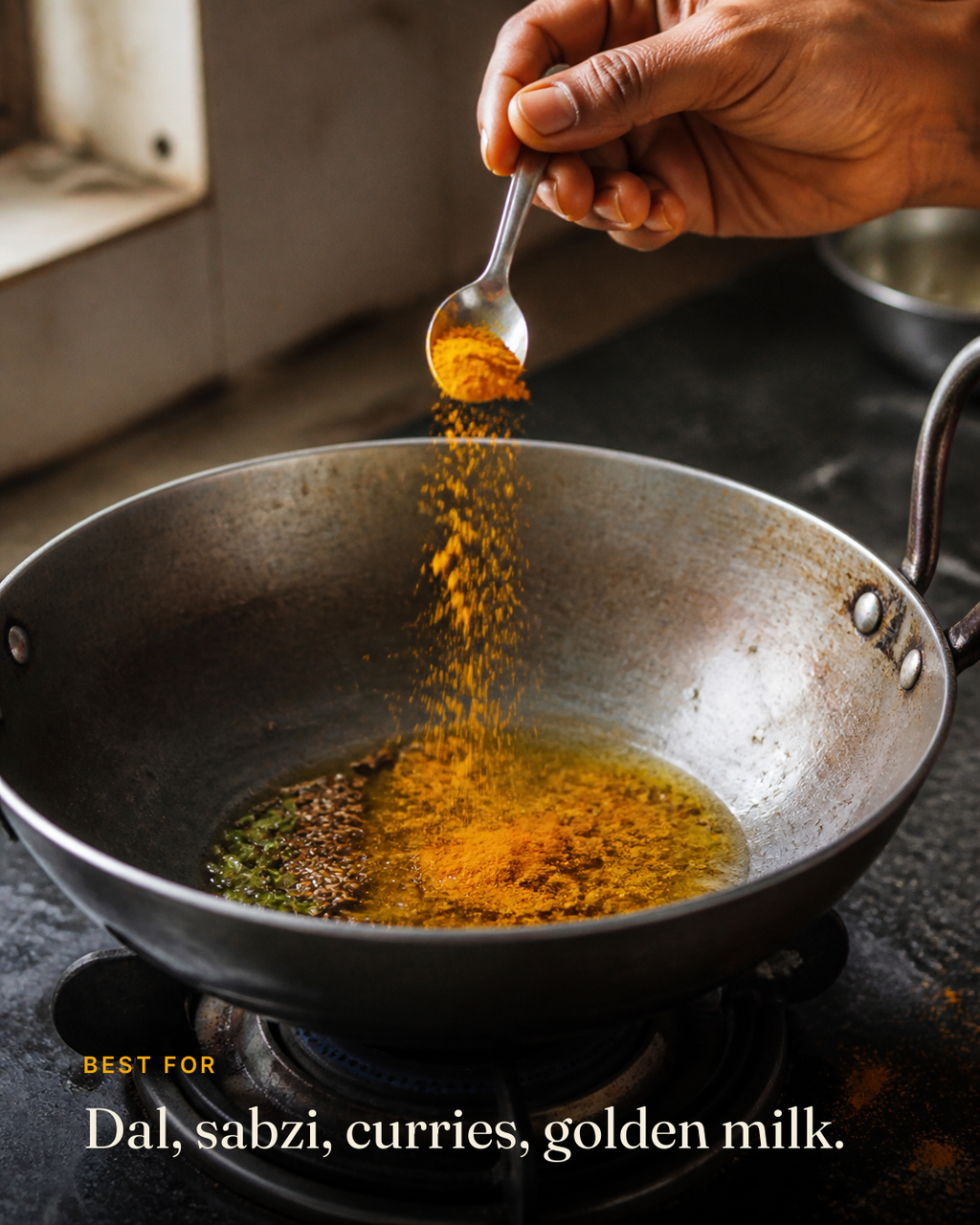 GetPured turmeric powder being tipped from a steel spoon into hot ghee in a kadai